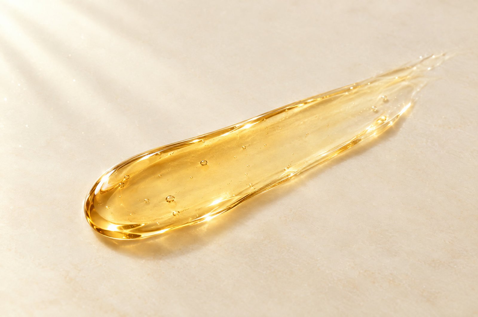 A swipe of golden serum on pale cream stone, catching soft morning light.